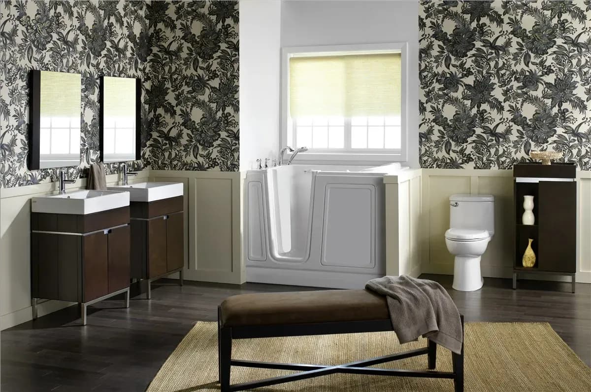 Modern bathroom with floral wallpaper, featuring a walk-in bathtub, double sinks with mirrors, a toilet, and a cushioned bench. The tone is elegant and serene.